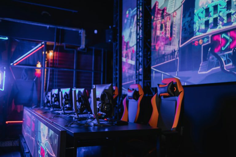 A high-tech gaming setup featuring multiple monitors and ergonomic chairs illuminated by neon lights.